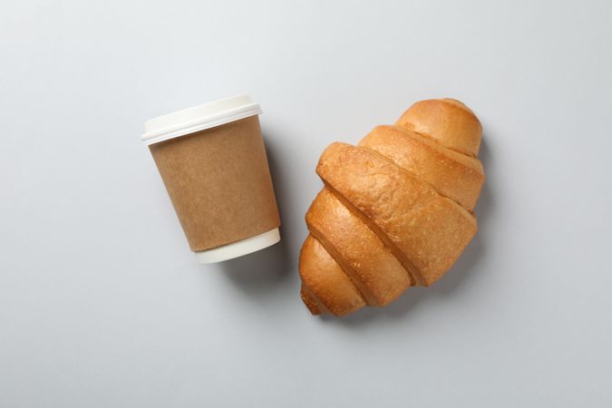 Croissant and cup of coffee on plain background, space for text, top view