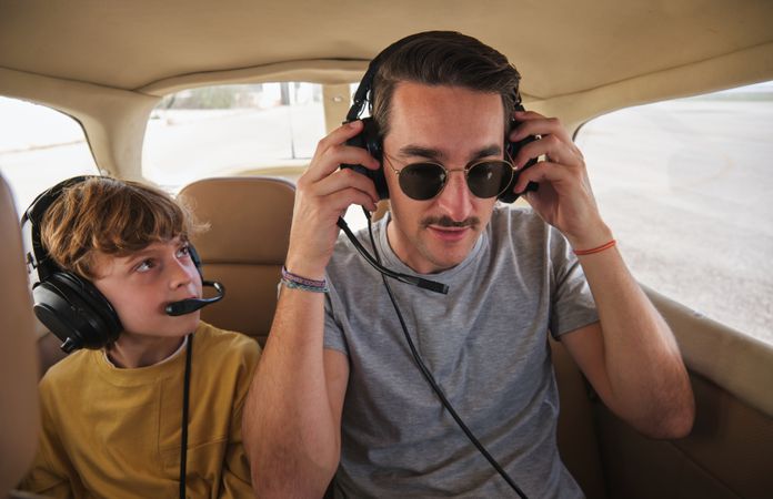 Young man with kid sitting in plane cabin and wearing headphones