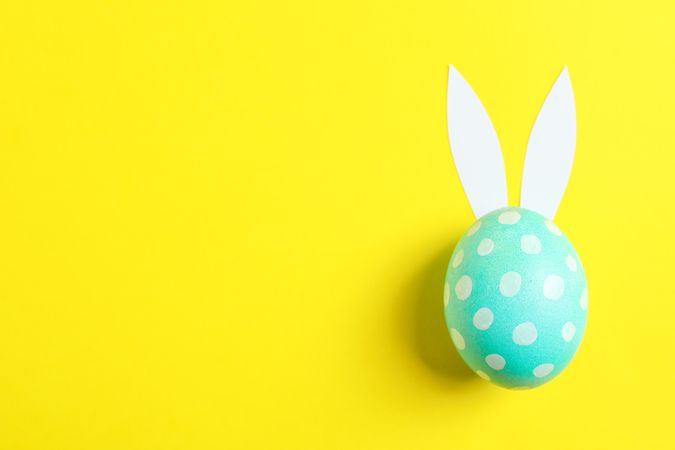 Decorated Easter egg with cute bunnies ears on yellow background. Space for text