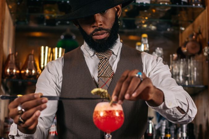 stylish Black bartender offering a customer a cocktail decorated with garnish in a traditional cocktail bar