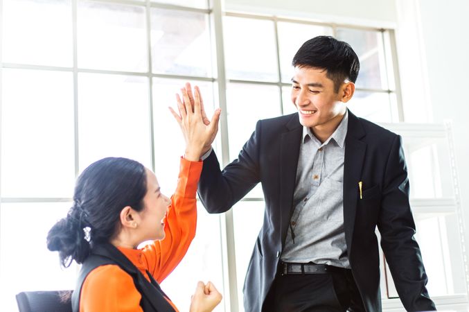 Happy successful Asian business man and woman giving high five for project success