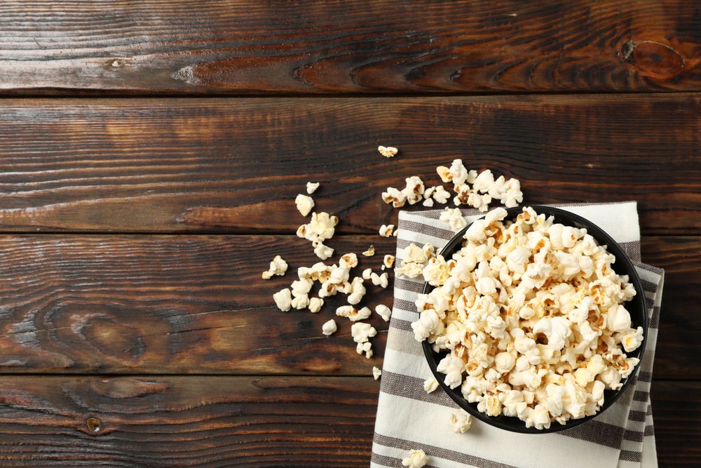 Towel and bowl with popcorn on wooden background, copy space