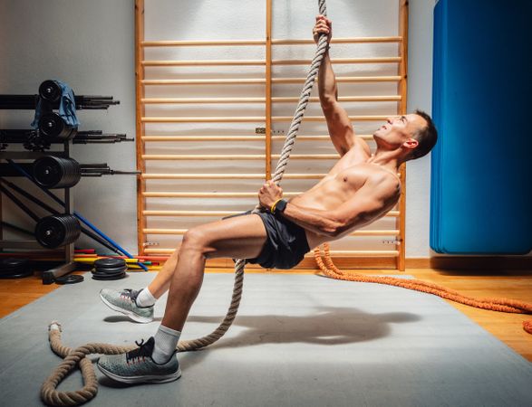 Muscular athlete climbing rope in gym