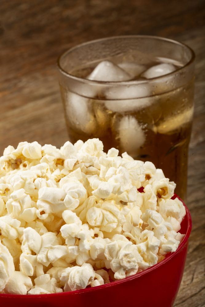 Bowl with salted popcorn and soda on the table.
