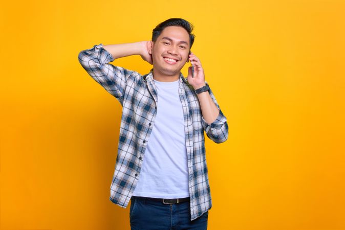 Smiling Asian male talking on phone in studio shoot with hand behind his head