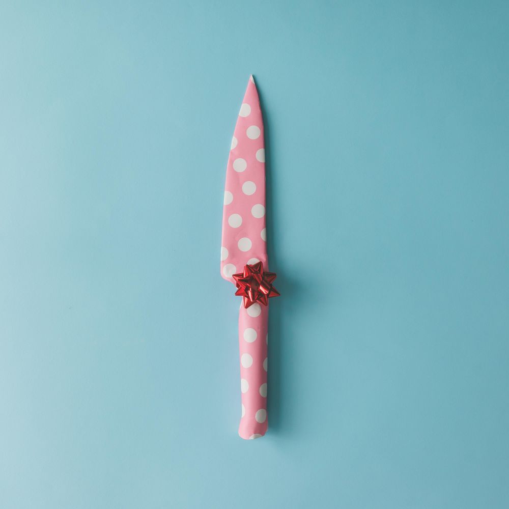 Knife wrapped in pink dotted paper with bow on blue background