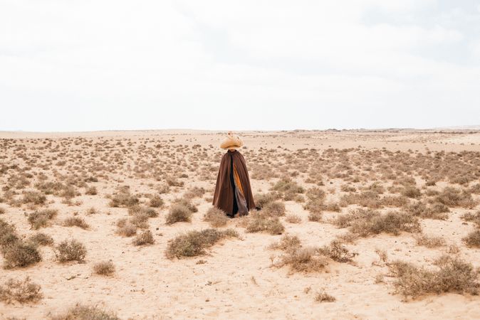 Person in long robes walking through arid landscape with basket on head