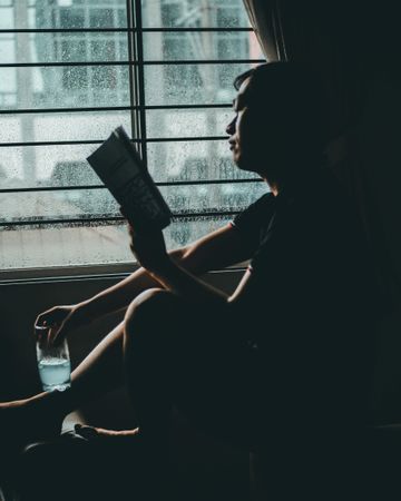 Silhouette of man reading book beside window