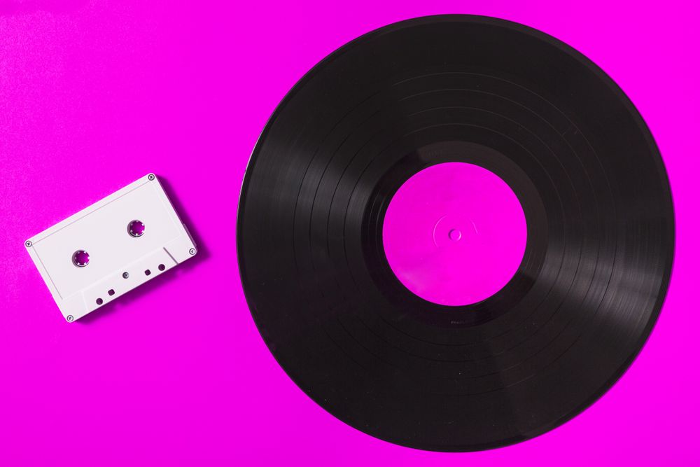 Audio cassette tape and vinyl record on pink background
