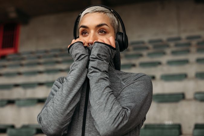 Woman in sweatshirt standing in a stadium listening to music