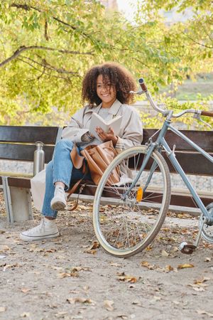 Cheerful Black woman with bicycle sitting on bench in park