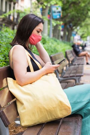Woman in mask using smartphone in city during coronavirus