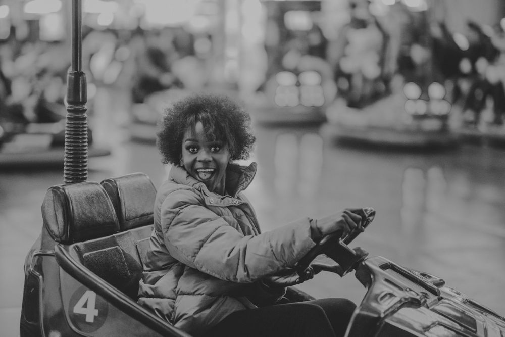 Excited Black woman riding car in amusement park