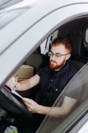 Courier filling papers while preparing for delivery of order to client in car