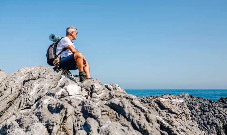 Mature man sitting on rocks and enjoying the view on an ocean hike