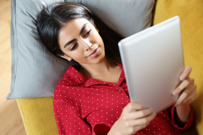 Female relaxing on sofa while reading a tablet