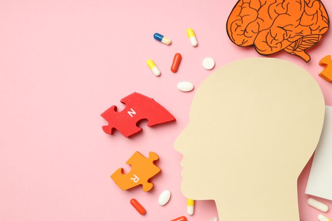 Paper cut out of side view of head with medications and puzzle pieces, close up with copy space