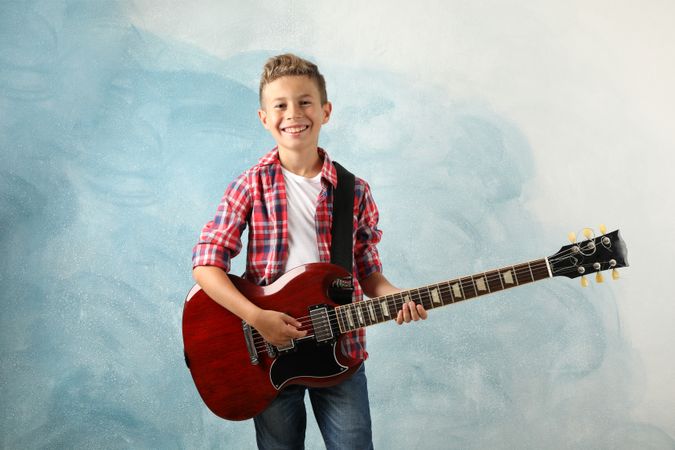 Happy boy with electric guitar on color background, space for text