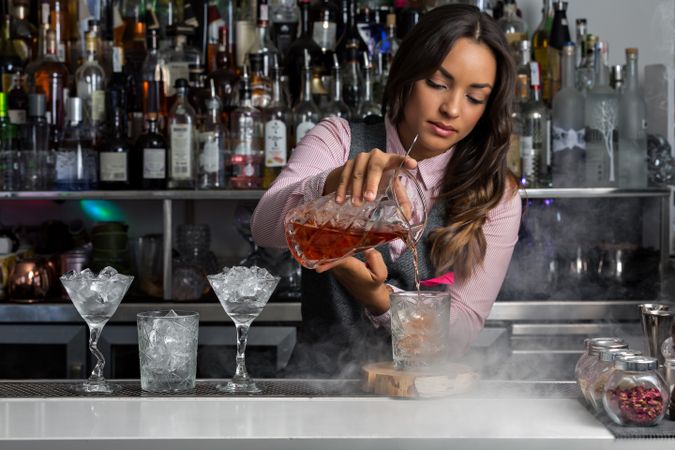 Bartender pouring stirred Negroni cocktail into an old-fashion glass