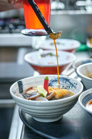 Person pouring sauce into bowl with noodle soup