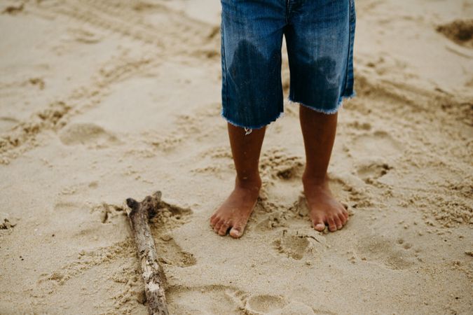 Crop child standing on sand near stick