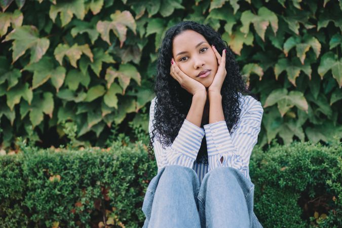 This is a thoughtful young woman dressed in casual attire, surrounded by lush greenery