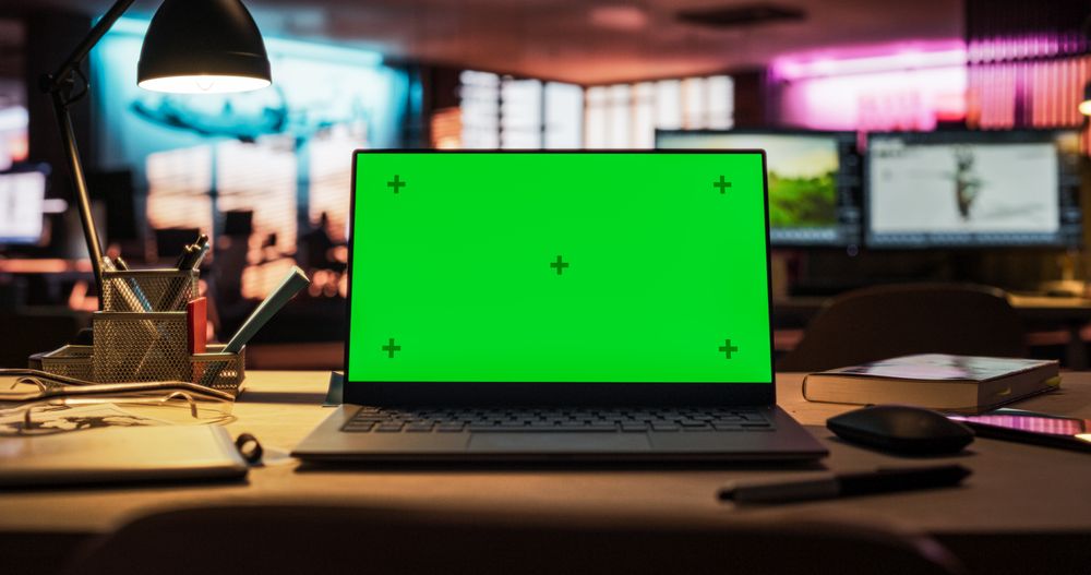 Laptop Computer Standing on a Wooden Desk with a Green Screen Chromakey Mock Up Display. Creative Office Working Station for Game Developer and Graphic Designer in Creative Agency