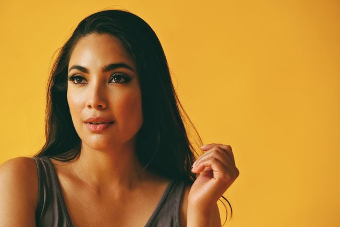 Wistful Hispanic woman looking away from camera in yellow room with her hand to her hair