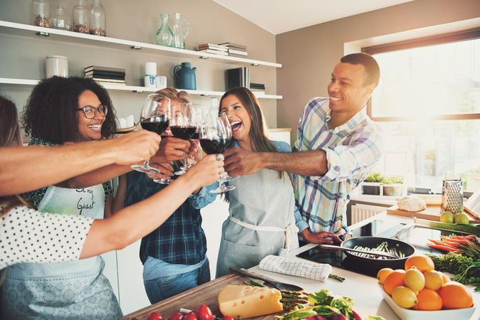 Multi-ethnic friends smiling with red wine while cooking dinner together