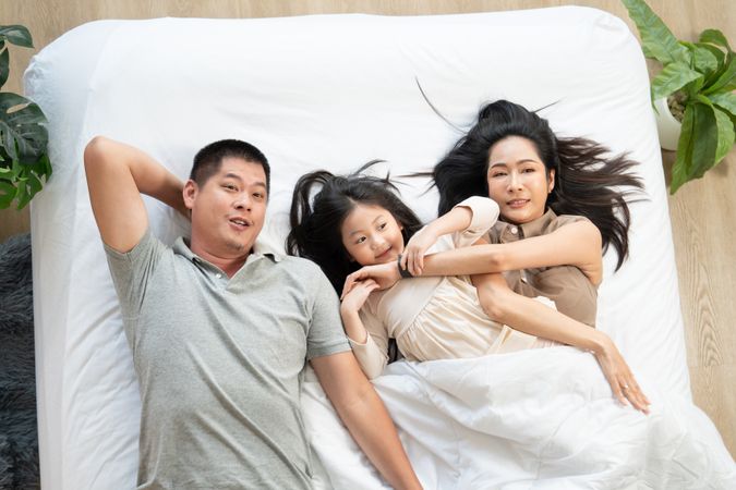 Top view of Asian family lying on bed and holding hands together.