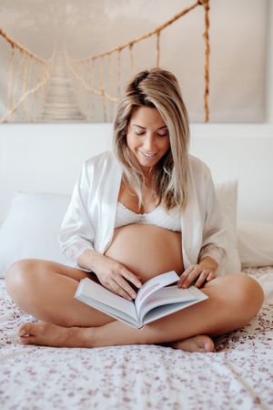Smiling pregnant woman reading book at home