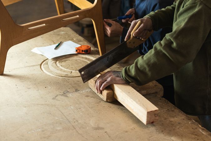 Joiner cutting wood with colleague measuring height