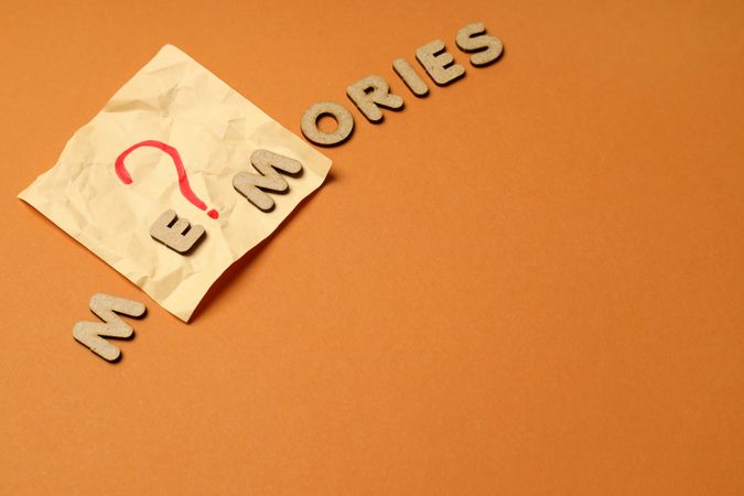 The word “Memories” written in cork on top of post it note on dusty orange background, copy space