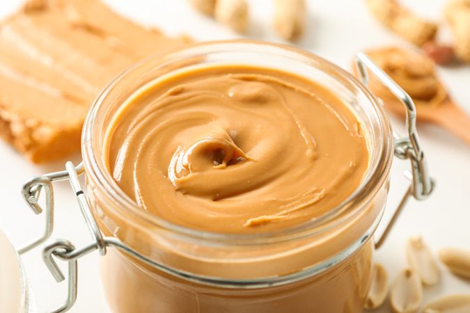 Composition with peanut butter sandwich, glass jar, peanut and spoon on light background, space for text and closeup