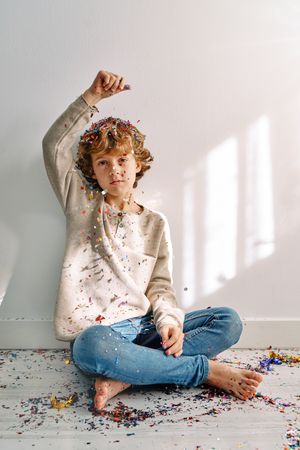 Cute little boy sitting on floor and strewing confetti