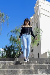 Young stylish woman wearing earphones spending free time outdoors standing listening to music looking down