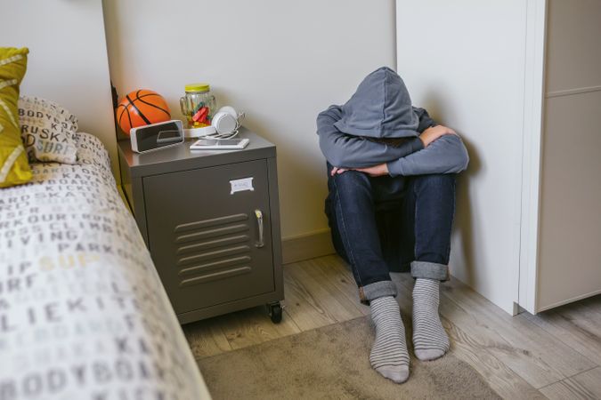 Teenager boy with anxiety sitting on the floor of his bedroom with his head resting