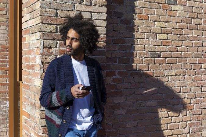 Black male using his smartphone with smile while leaning on a wall outdoors on sunny day