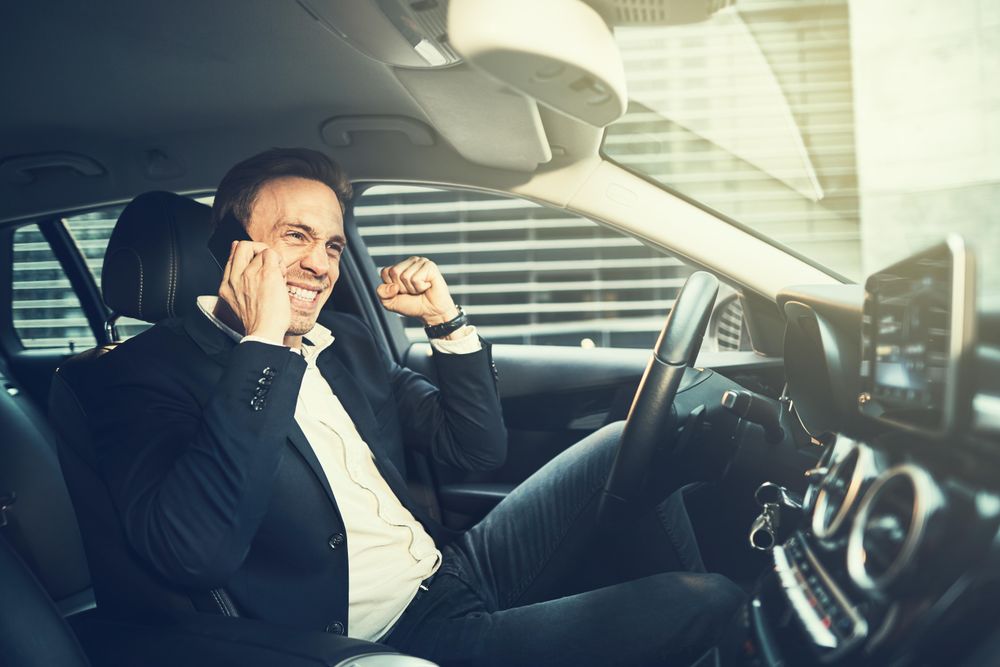 Happy man making a celebratory fist while talking on his cell phone in a vehicle