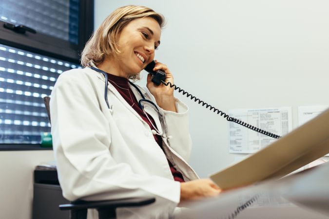 Female doctor reading medical reports and  talking on phone at clinic