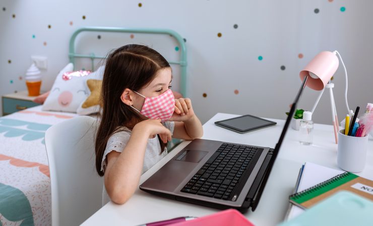 Little girl with mask using laptop