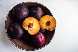 Top view of bowl of fresh ripe plums on kitchen counter