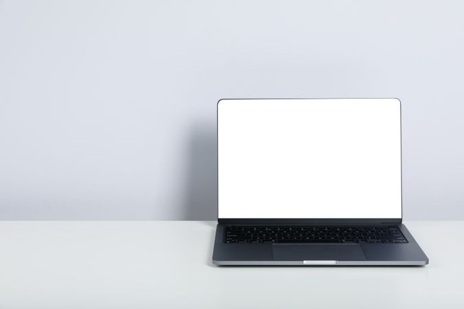 Opened silver laptop with mockup screen and keyboard on desk with copy space