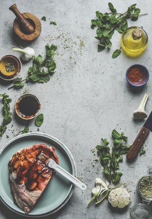 Raw marinated lamb on plate at kitchen table with mint, spices, garlic, oil, mortar and pestle and kitchen utensils