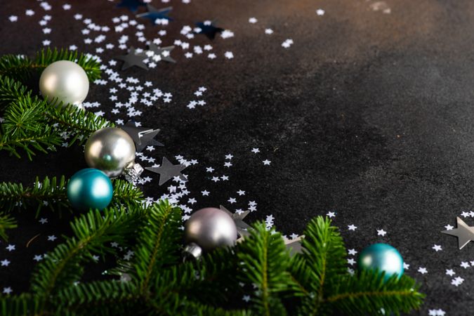 Christmas card concept of blue and silver baubles on table with pine and star confetti with copy space