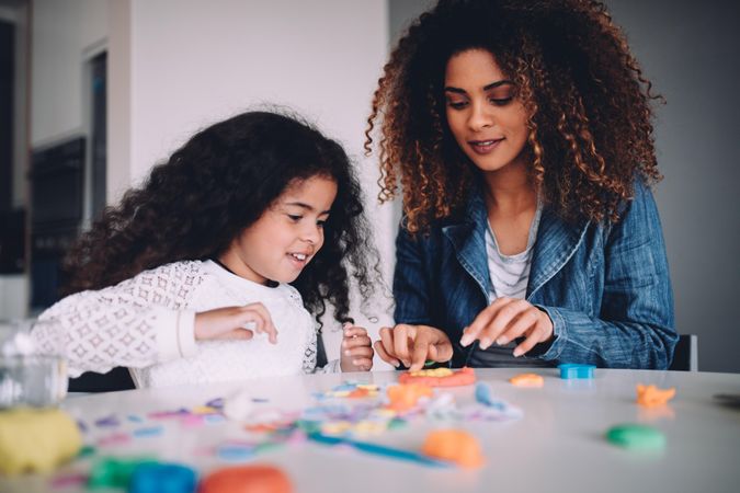 Mother and daughter happily playing with playdough at a table