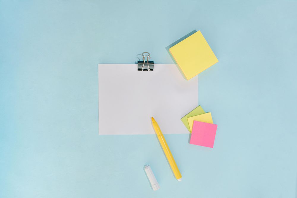 Flat lay of pens and note pad paper on blue background