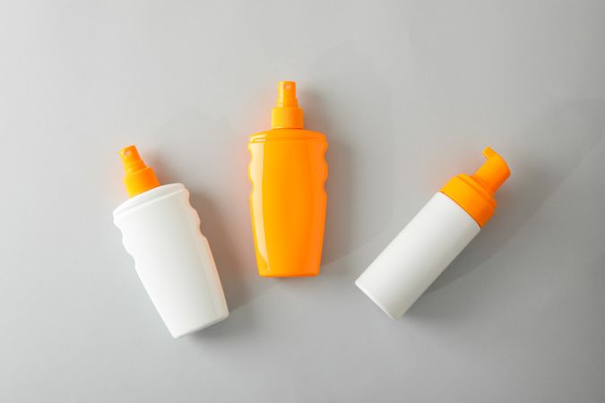 Flat lay composition with sunscreen sprays on grey background. Space for text, top view