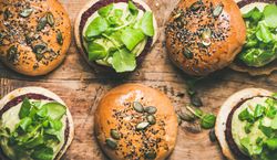 Fresh vegan burgers on seeded buns arranged on wooden board