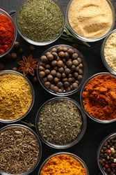 Vertical composition of glass bowls full of spices on dark table